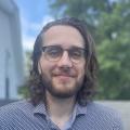 Eric, on a rooftop with long hair, glasses, and a beard