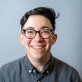 Smiling white person with short dark hair and dark-rimmed glasses