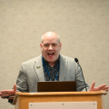 a picture of Matthew Saunders at a podium speaking.