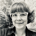 A middle-age woman with short wavy hair and cute glasses