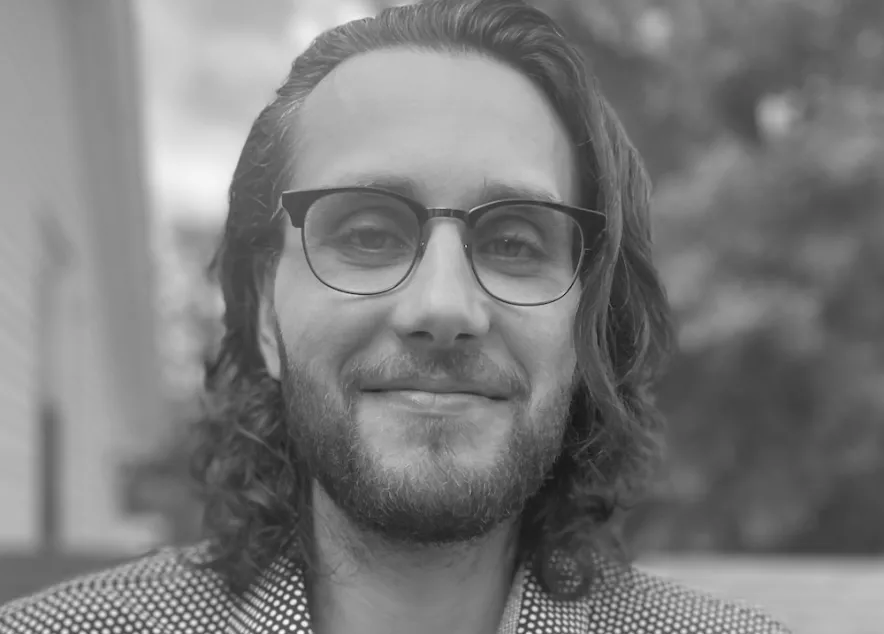 Eric, on a rooftop with long hair, glasses, and a beard