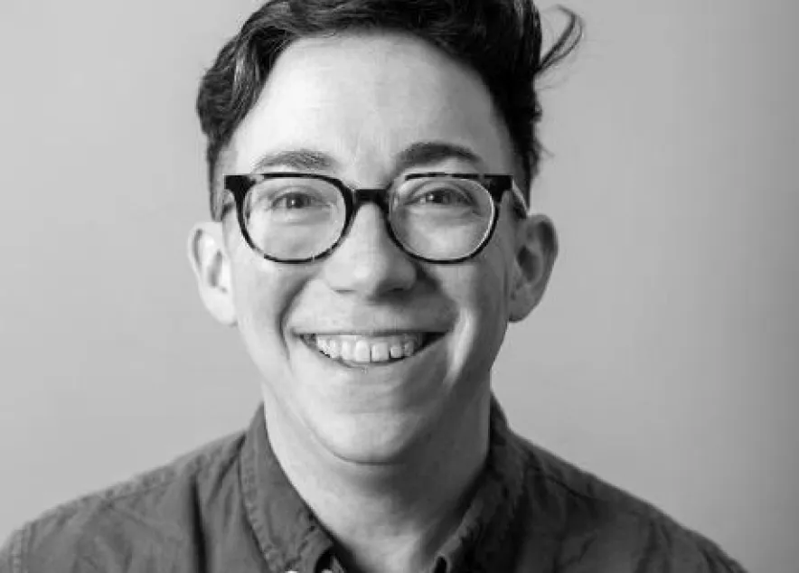 Smiling white person with short dark hair and dark-rimmed glasses
