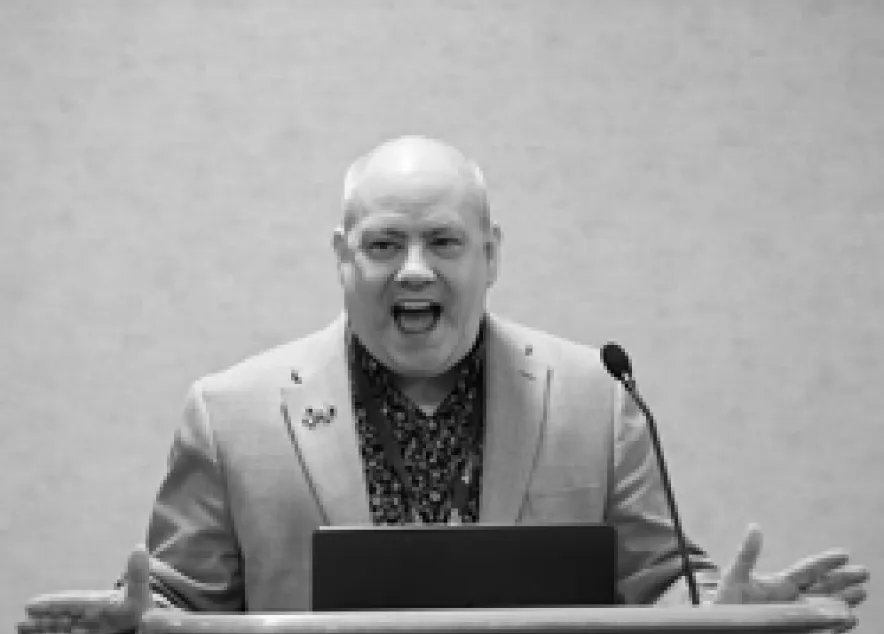 a picture of Matthew Saunders at a podium speaking.