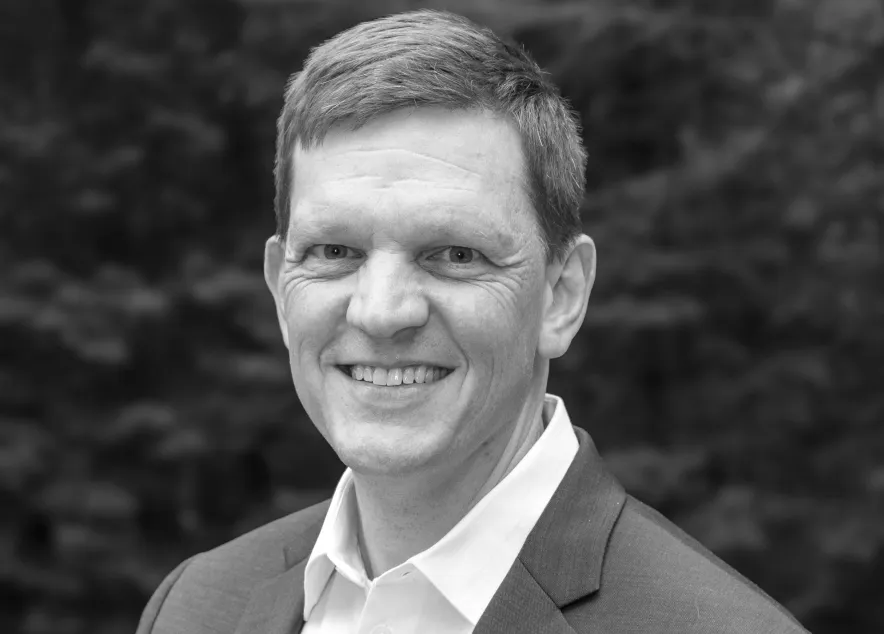 Portrait of a smiling man with light brown hair wearing a white shirt and blue jacket