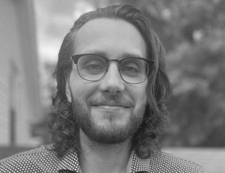 Eric, on a rooftop with long hair, glasses, and a beard