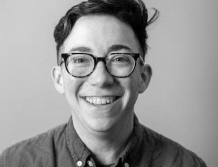 Smiling white person with short dark hair and dark-rimmed glasses