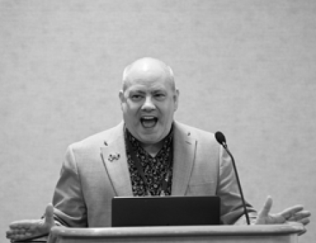 a picture of Matthew Saunders at a podium speaking.