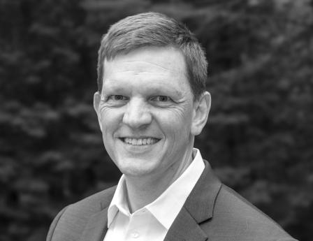Portrait of a smiling man with light brown hair wearing a white shirt and blue jacket